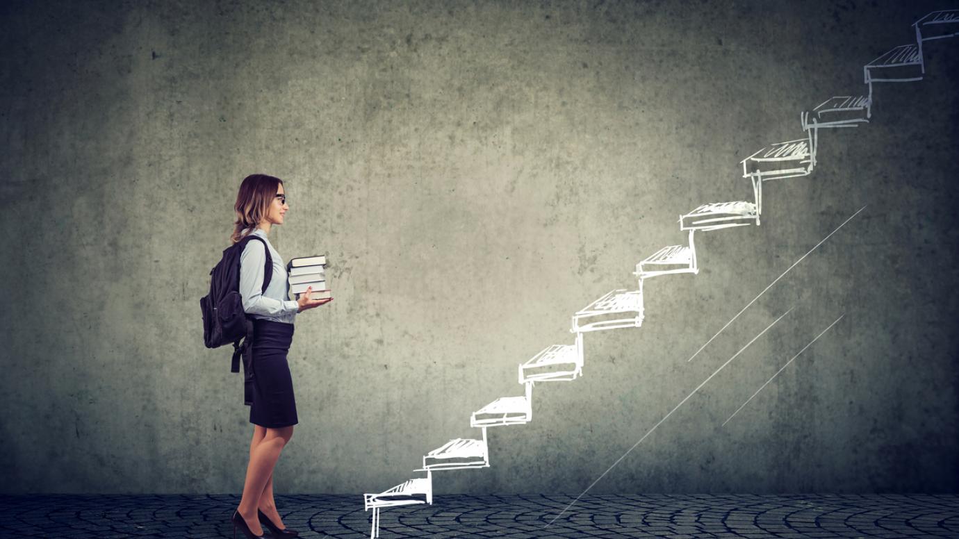 Female student with books standing on the stairs of education leading to success