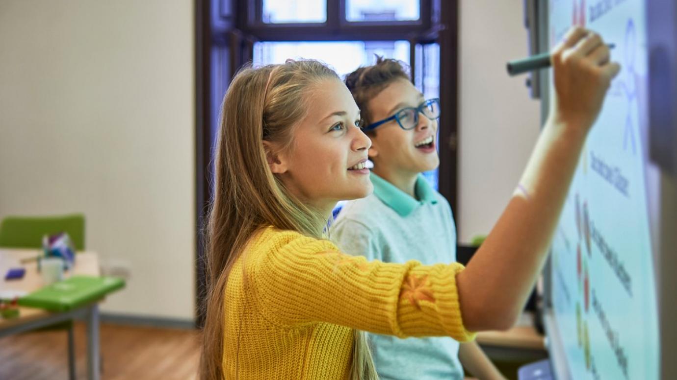 Two children in a classroom using an interactive whiteboard