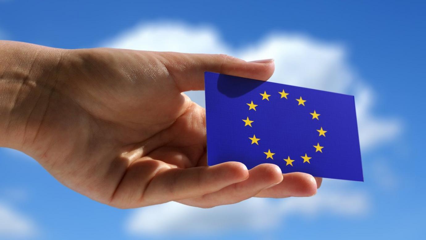 Hand holding a small, blue card containing the EU flag to the sky