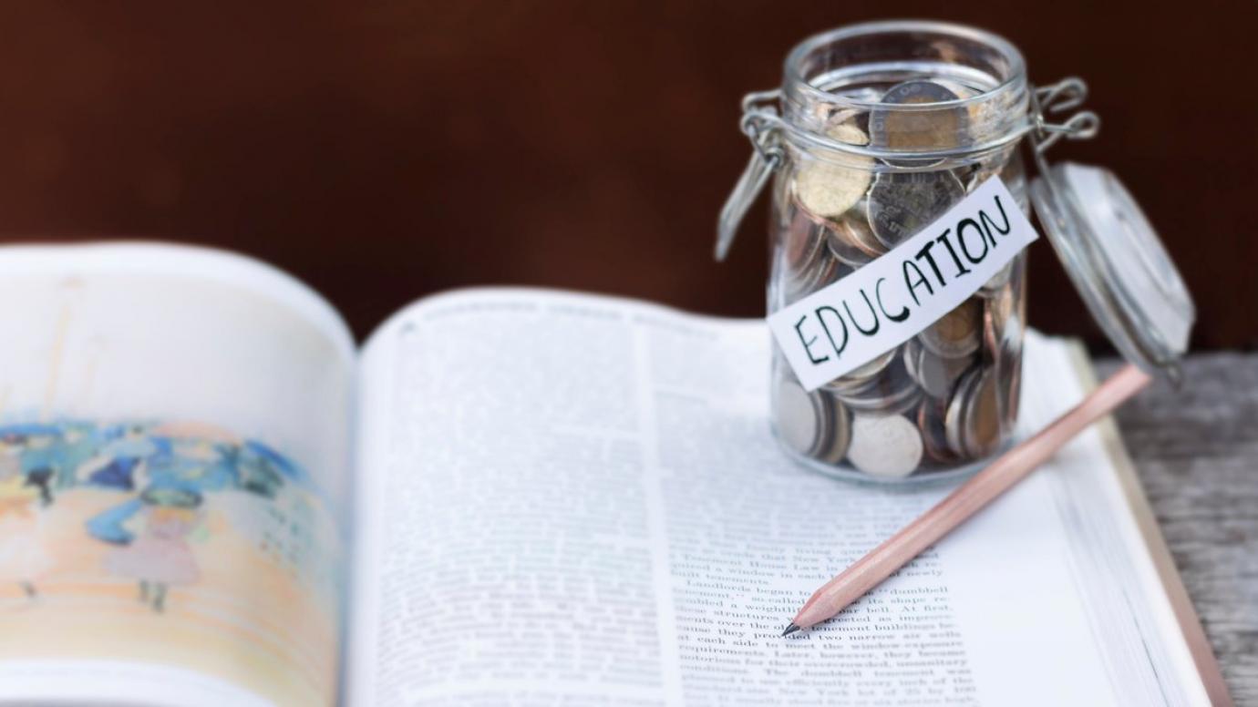 Coin jar placed on a book with the word 'education' written on it.