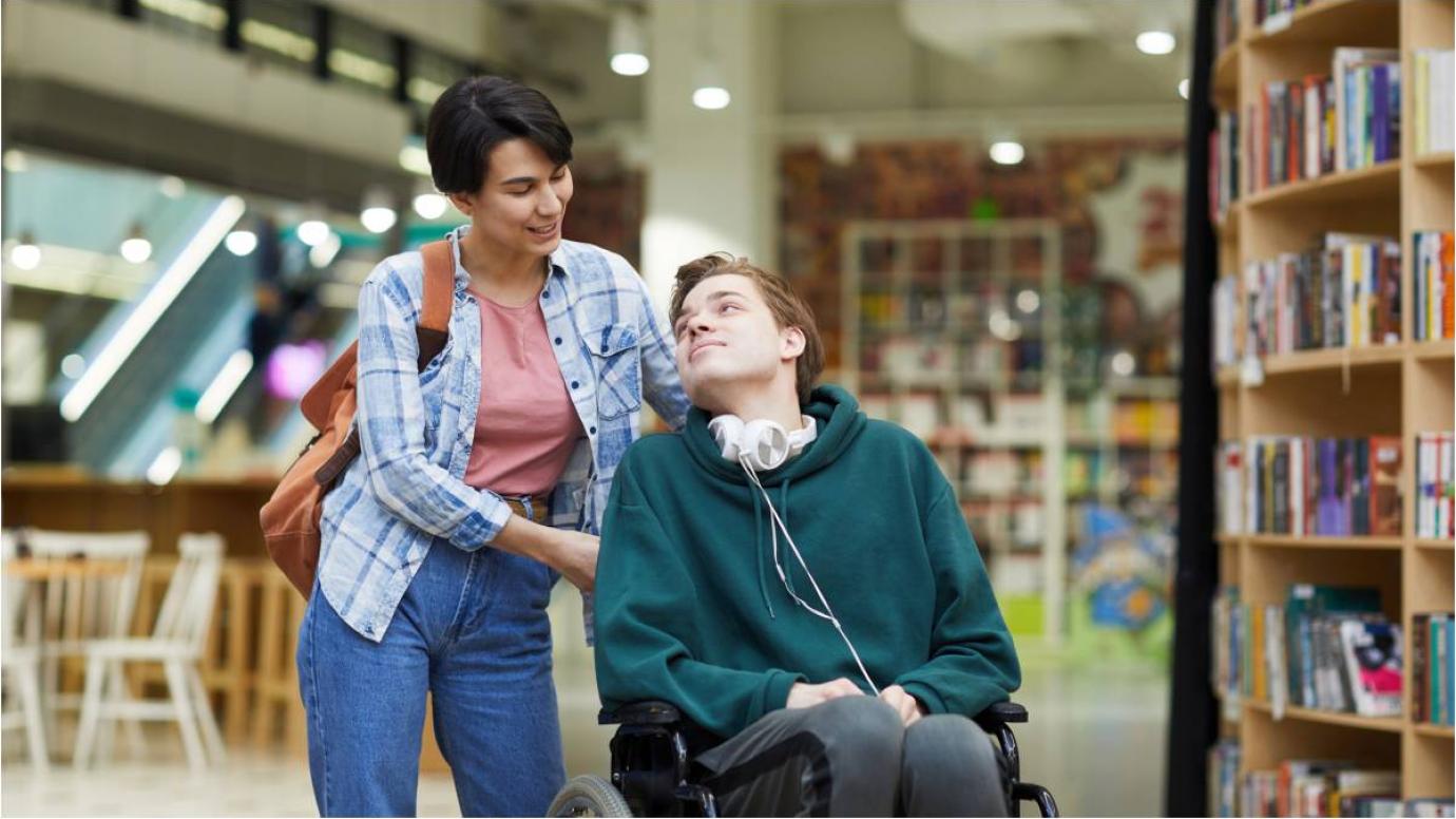 Student with disabilities in a library with a classmate assistant