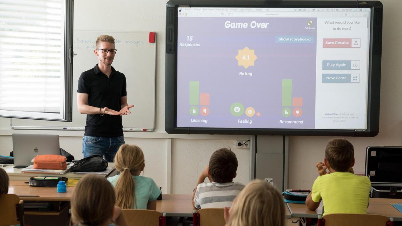 A teacher with a large digital board in a classroom with some children