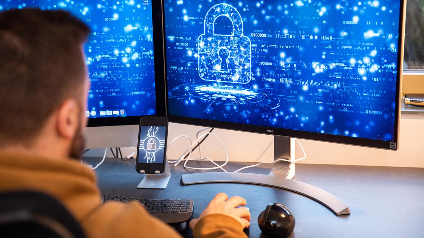 Cybersecurity expert sitting in front of 2 computer screens and a smartphone
