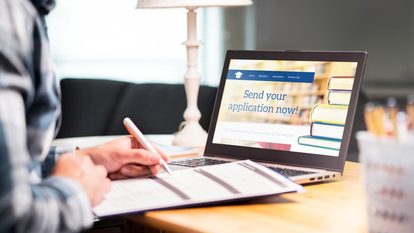 Person sitting behind laptop. The laptop shows an application page of the higher education institution. Person is filling in a document.