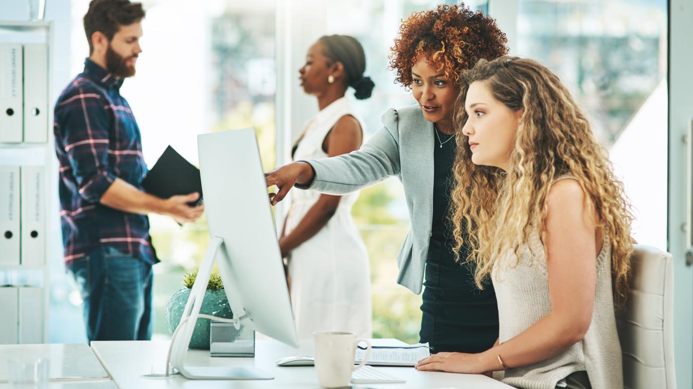 Female office worker giving IT guidance to young trainee