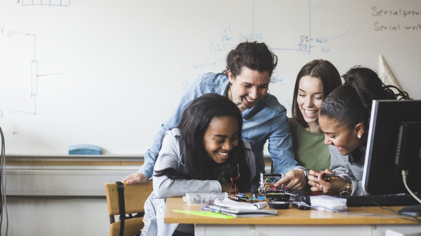 Group of female teacher and diverse female pupils working on circuit device