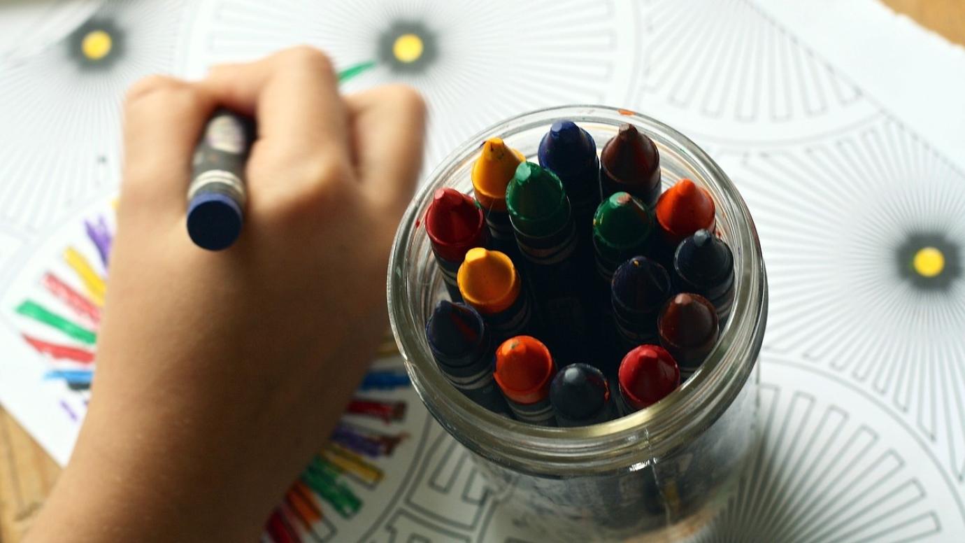 A child's hand drawing a multicoloured pattern with some crayons.