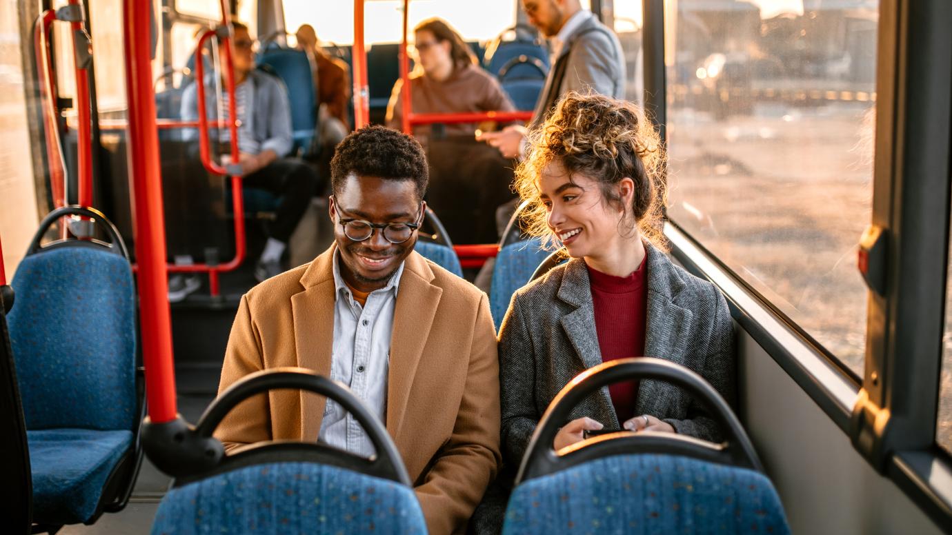 Smiling young Black man sitting on a bus next to smiling young white female