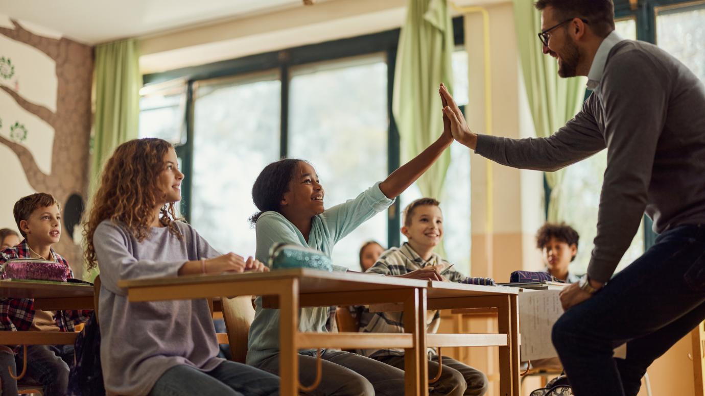 Male teacher giving a high five to a young female student of colour 