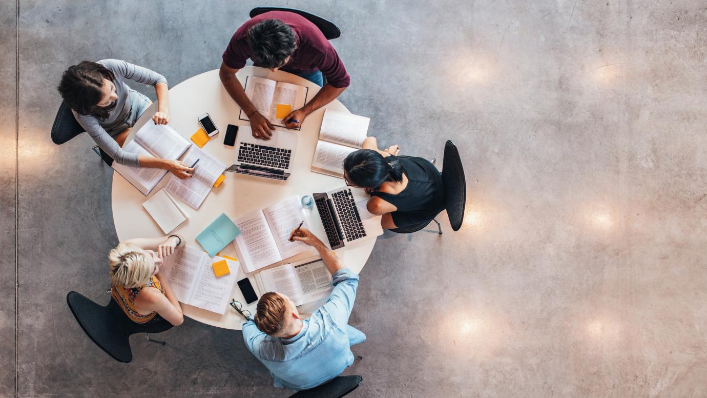 Group of diverse students working together with laptops, books and notepads around a table