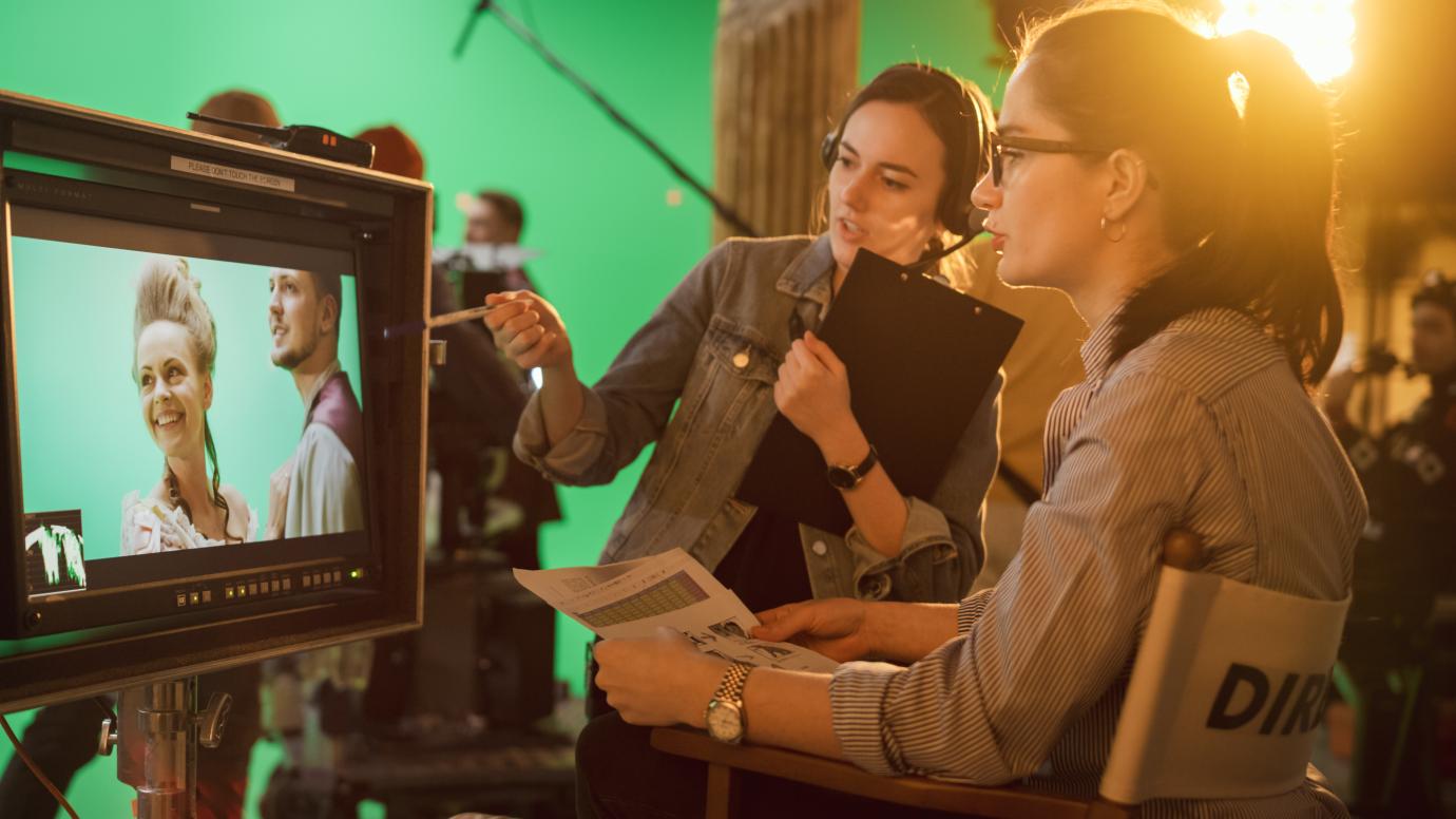 Female director and assistant discussing behind the camera on movie set