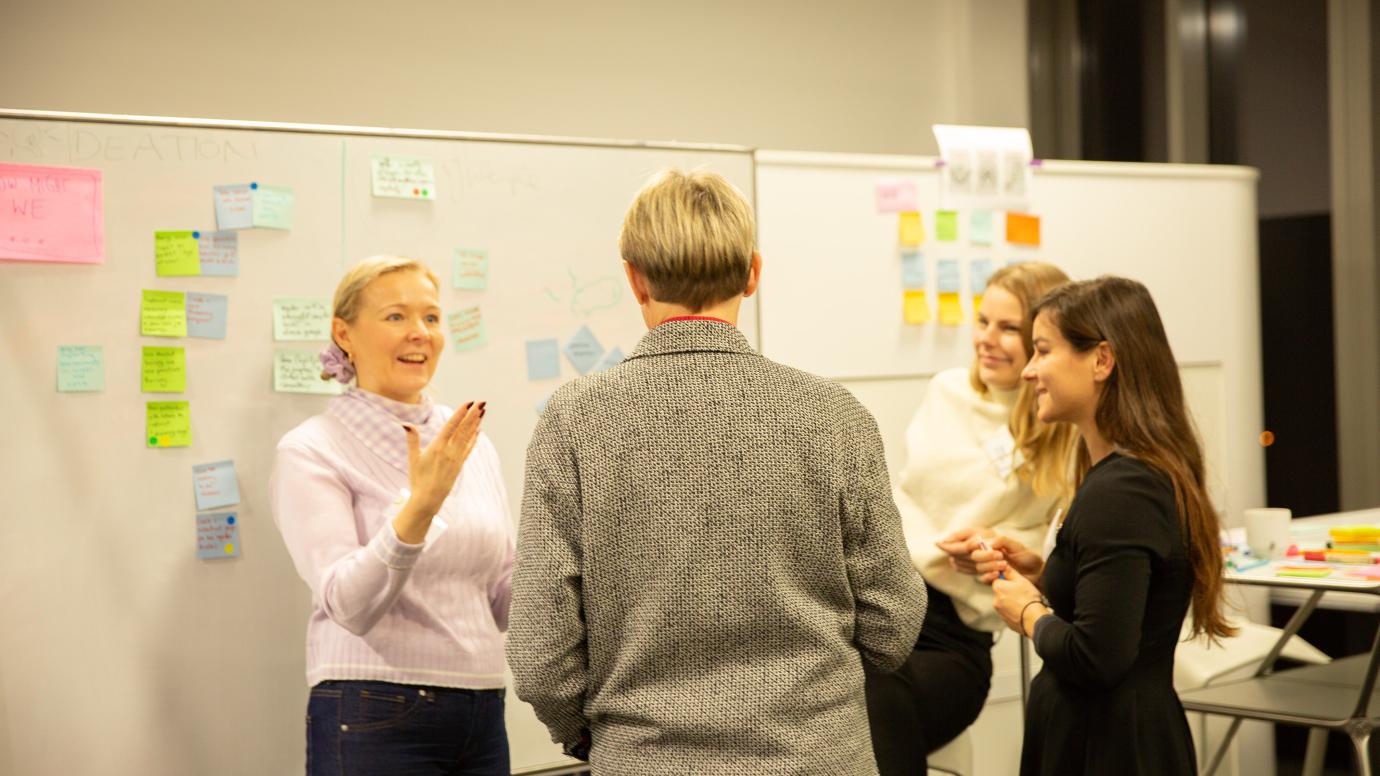 Group of women discussing in front of a whiteboard filled with sticky notes
