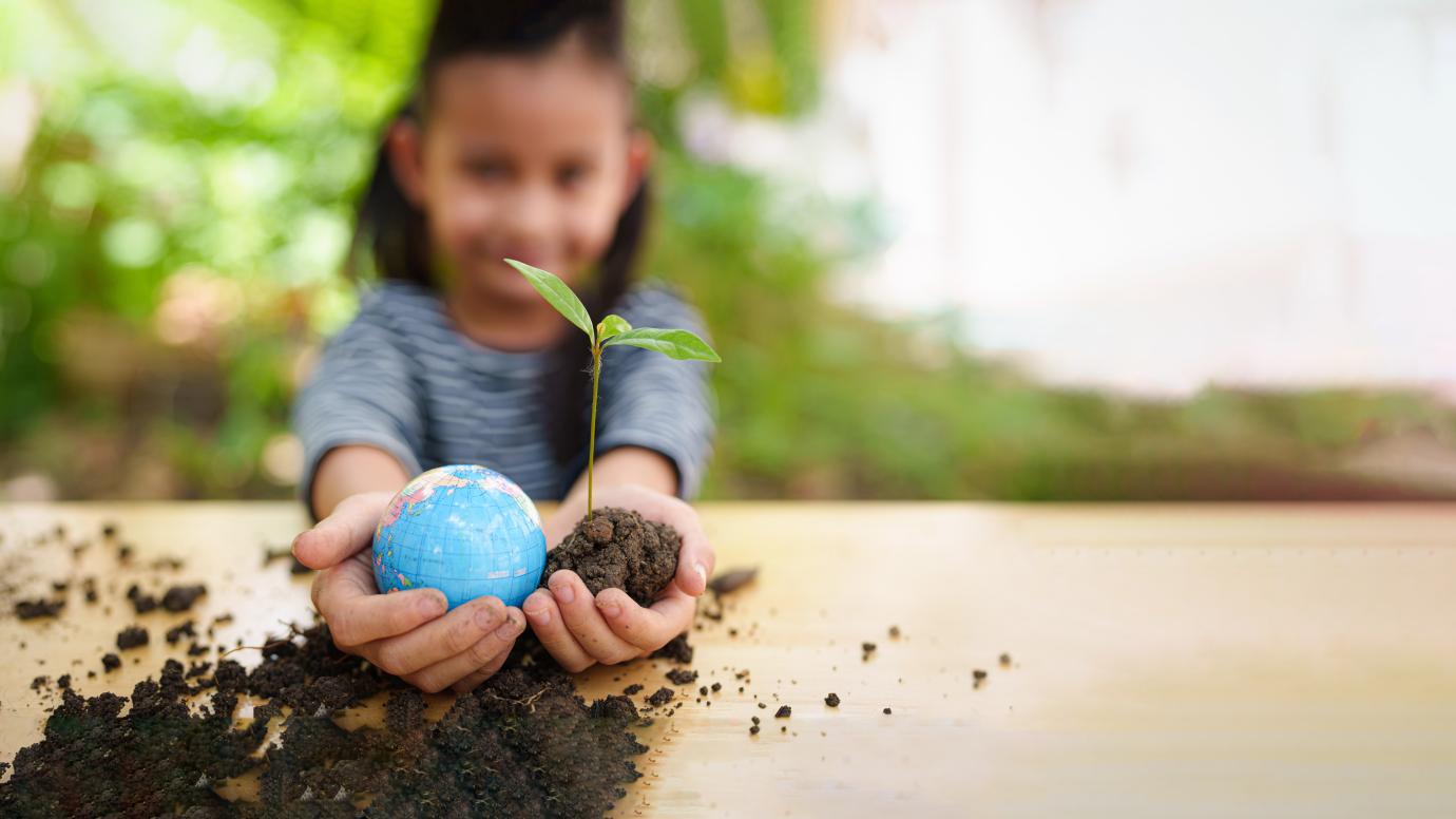 Young female pupil holding a seedling coming out of soil and a small Earth globe