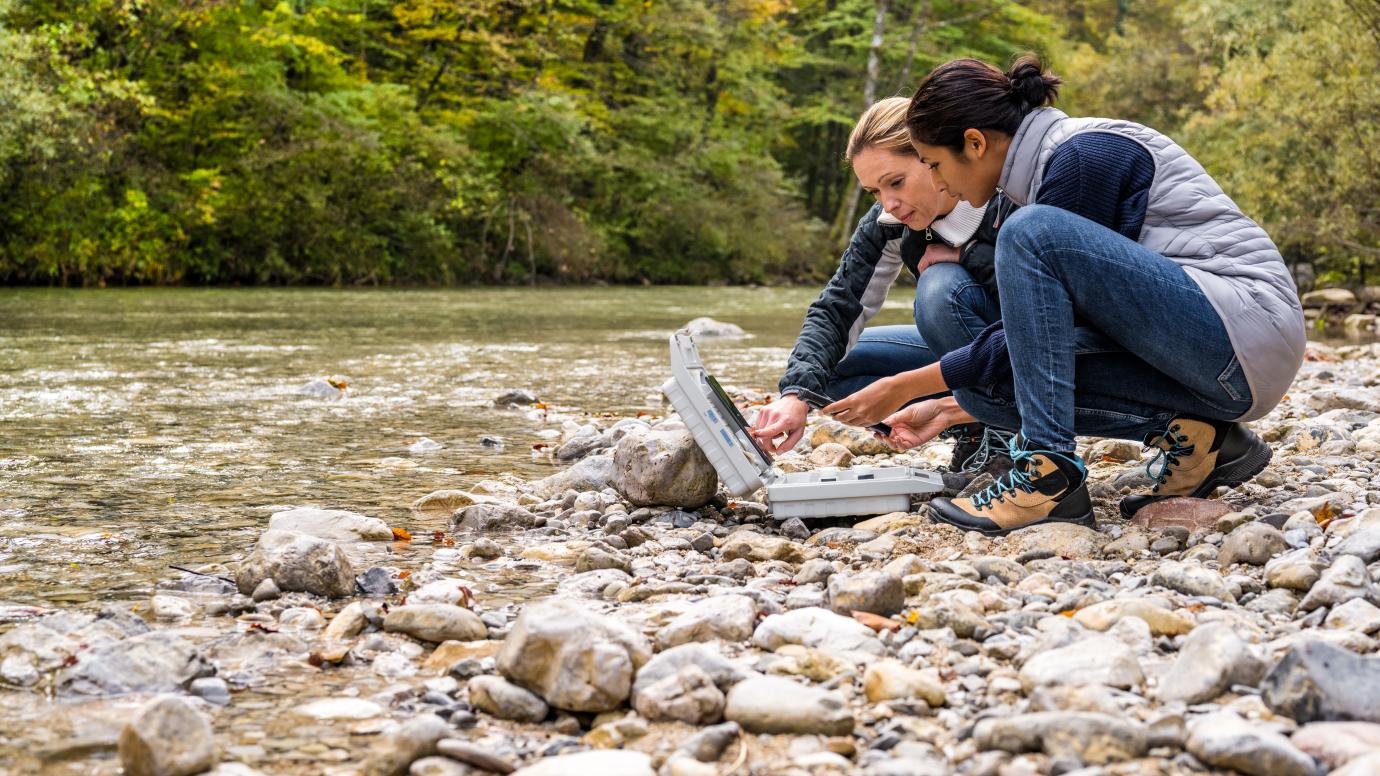 2 female biologists evaluating water samples next to riverbed