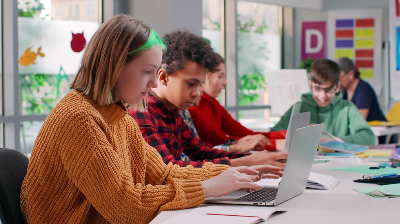 Multiethnic teenage students type on laptop in modern classroom