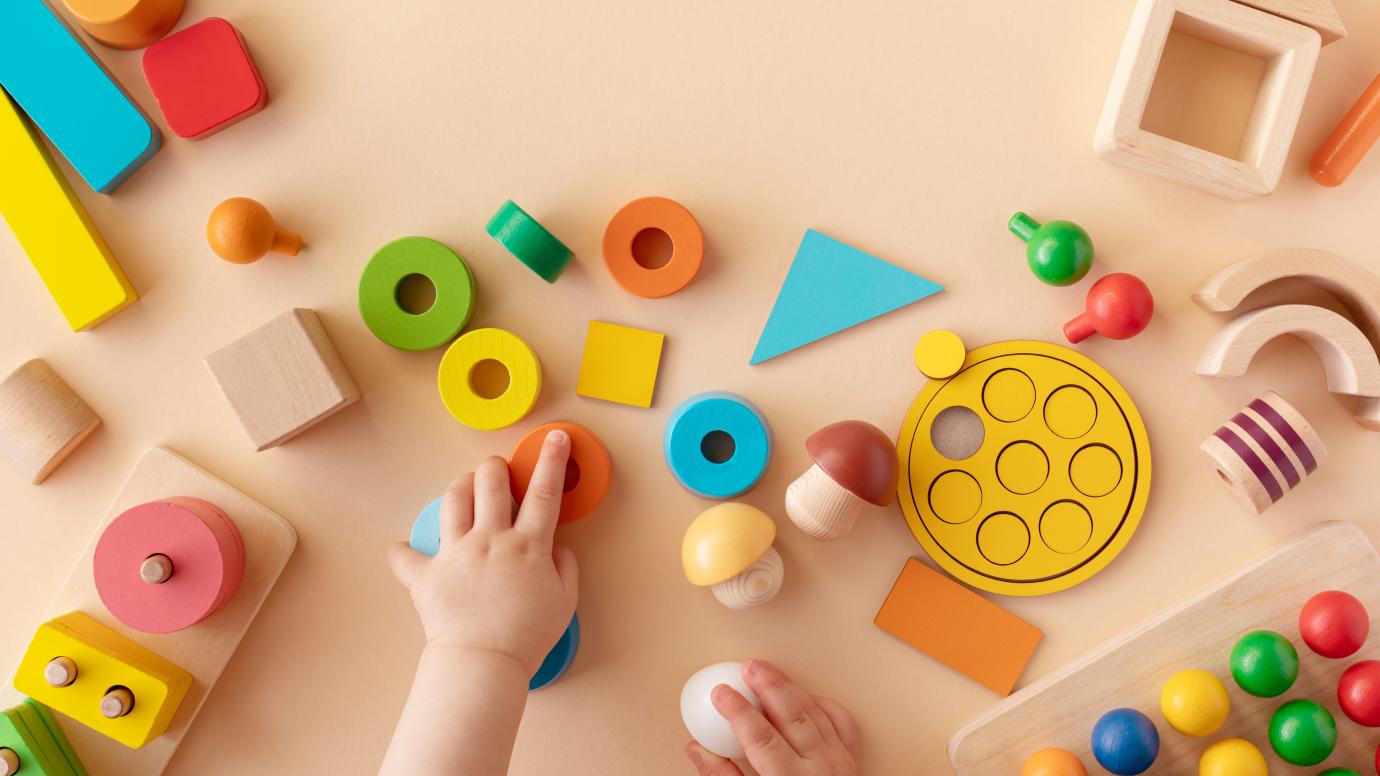 Baby hands with colorful wooden toys on table from above